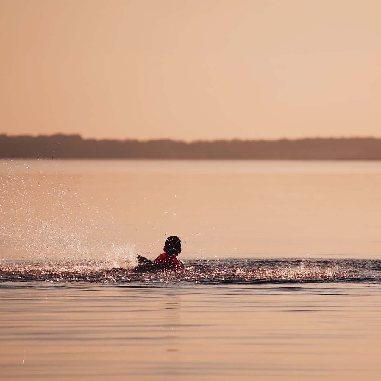Boy swimming in the river at sunset. Silhouette of a child is splashing happily in the evening water outdoors. Slow motion.