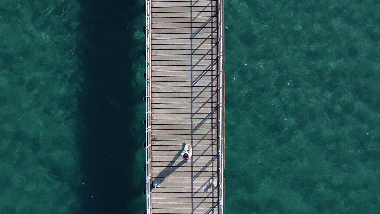 tiro aéreo ascendente, mirando hacia abajo a una niña caminando por un muelle de madera junto al mar