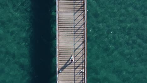 rising aerial shot, looking down on a little girl walking along a wood pier by the sea