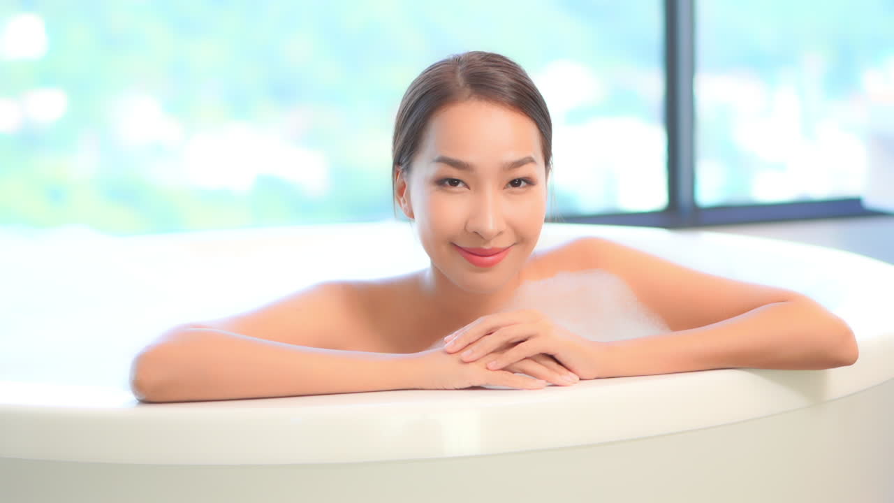 Close-up on an Asian woman taking bath with foam turning her sight from side to the camera