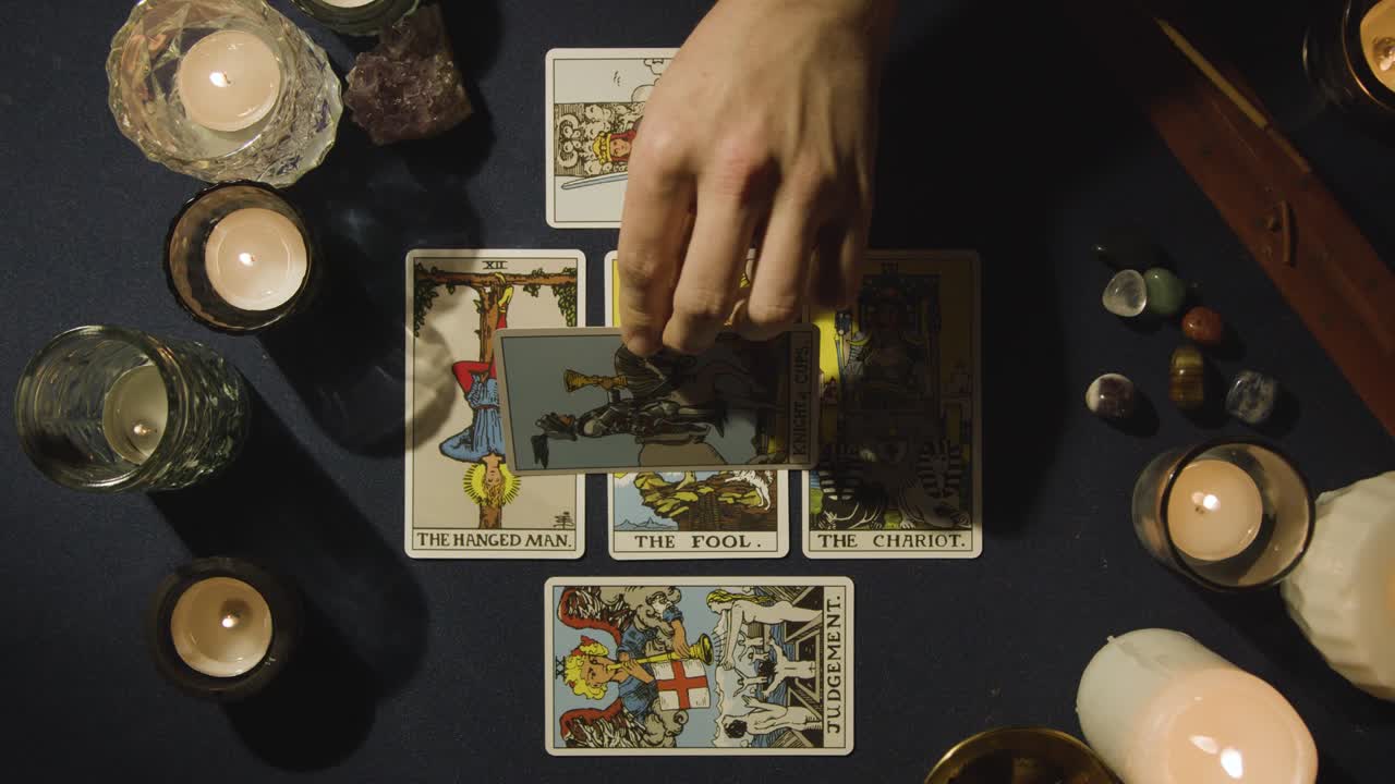 toma aérea de una persona que da lectura de cartas del tarot colocando cartas en la mesa con velas y cristales