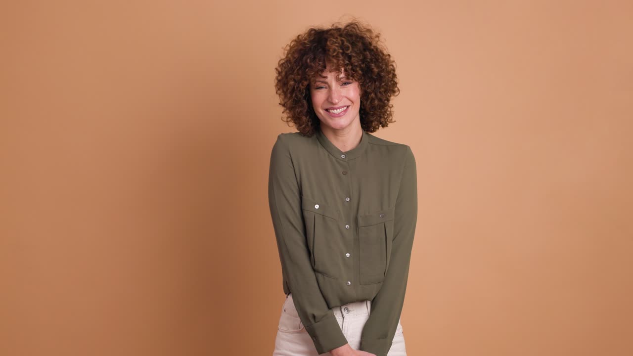 Smiling standing young curly haired woman on beige background
