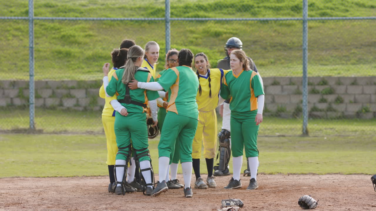 Multiracial female baseball players and white male umpire huddling and shaking hands on a pitch