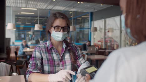 cliente femenina con máscara médica y guantes paga con tarjeta de crédito en una cafetería de comida rápida. en tiempo real