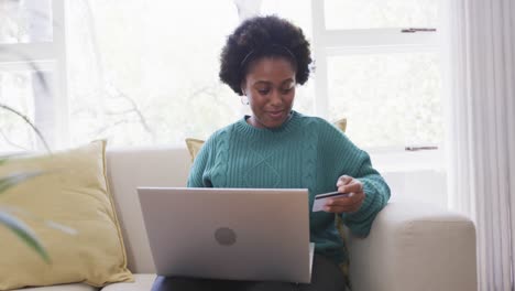 happy african american woman making payment using credit card and laptop at home, slow motion