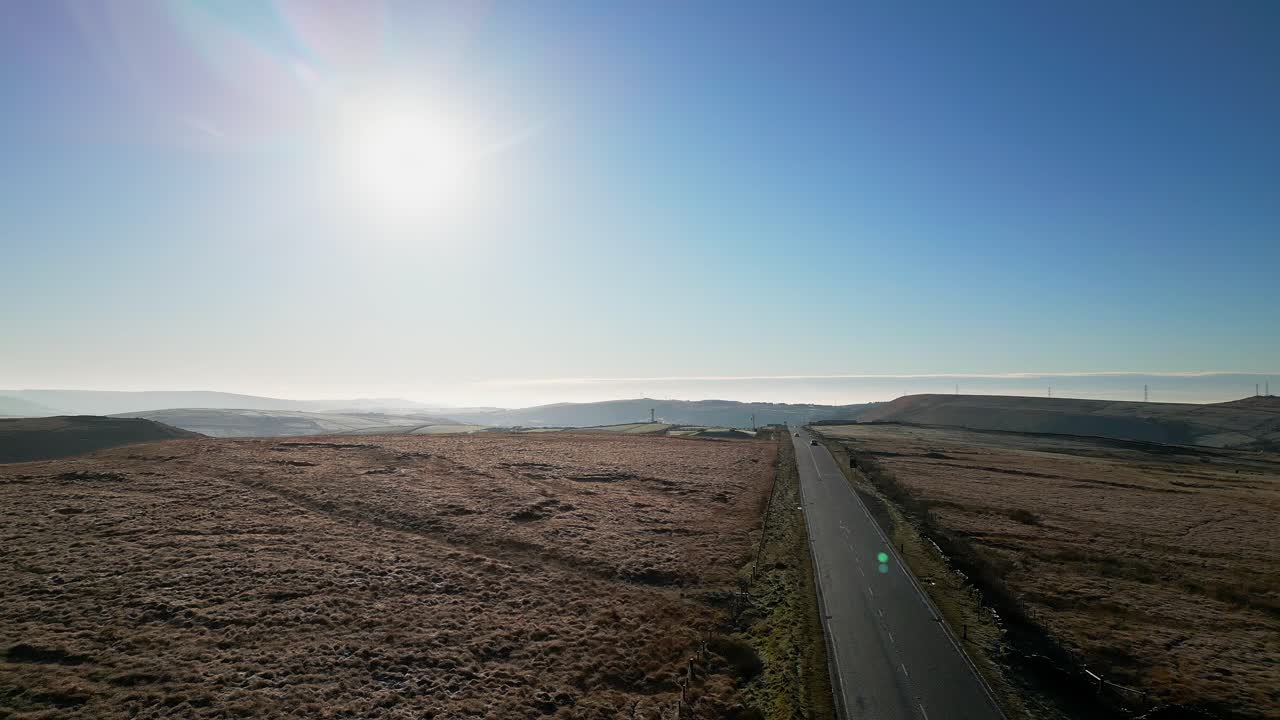 태양이 하늘에 낮게 깔리고 렌즈 플레어가 보이는 시골길을 달리는 차들