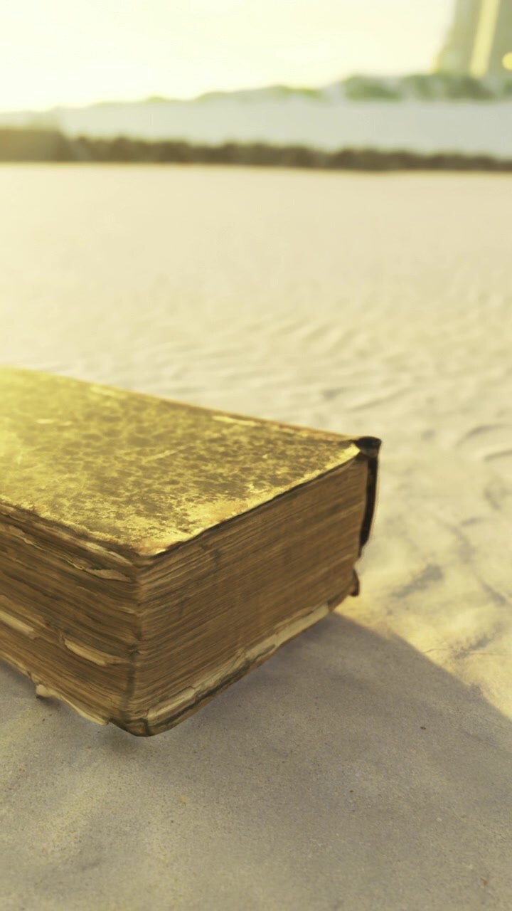 Old book rests on sand during sunset near water edge in bright light
