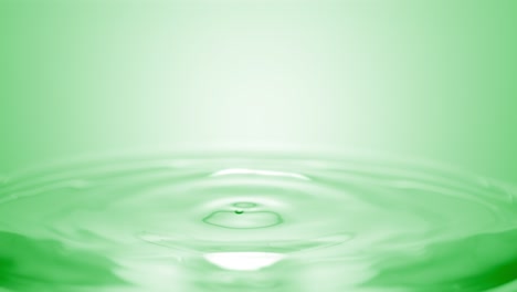 green drop falls down on surface of clear fluid creating circles