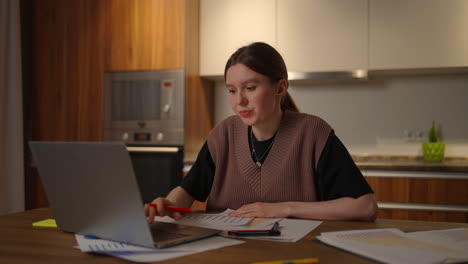 Portrait-of-a-woman-working-remotely-in-a-home-office-at-a-desk-with-a-laptop-and-notes-data-on-a-graph-business-economist-analyst.-Writes-down-makes-notes