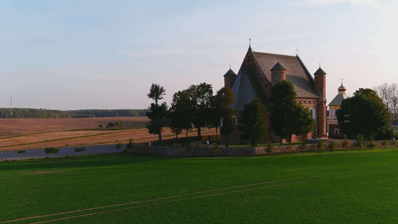Ripresa con drone di una storica chiesa ortodossa con alberi e campi rurali in Bielorussia durante la calda luce serale.