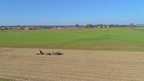 Luftaufnahme-Eines-Amischen-Mannes-Und-Einer-Frau,-Die-An-Einem-Sonnigen-Herbsttag-Maisstroh-Ernten-Und-Auf-Plätzen-Mit-Von-Pferden-Gezogener-Ausrüstung-Aussteigen