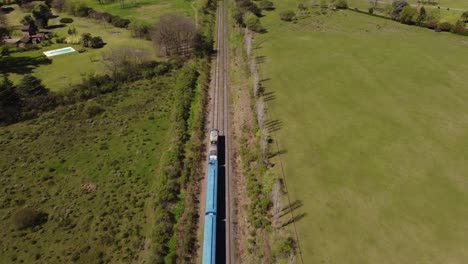 Toma-Aérea-De-Un-Tren-Azul-Conduciendo-Entre-El-Verde-Paisaje-Rural-De-Buenos-Aires