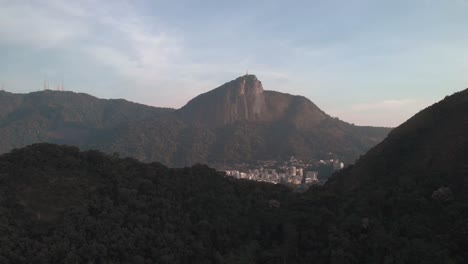 Amanecer-Vista-Aérea-Hacia-Atrás-De-La-Montaña-Corcovado-En-Río-De-Janeiro-Que-Revela-Una-Cadena-Montañosa-En-Primer-Plano-En-Otra-Parte-De-La-Ciudad-Con-Edificios-Residenciales-De-Gran-Altura-En-El-Frente