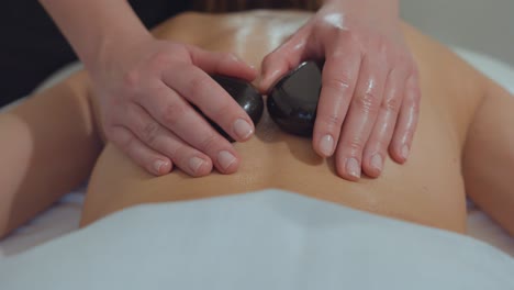 slow motion shot of a masseuse using hot stones on a womans back