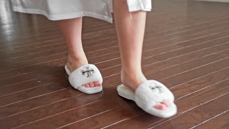 Morning-of-the-wedding-bride-is-in-a-white-robe-walking-towards-her-wedding-dres-wearing-slippers-with-Cole-Haan-logo-on-them