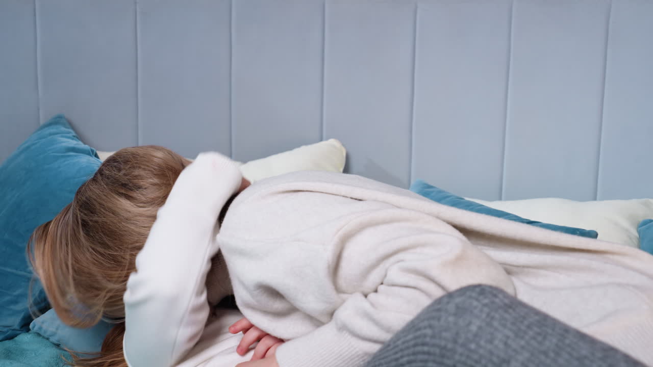 Smiling woman relaxing on bed holding playful girl with notebook raised above face, sharing tender bonding moment filled with laughter, warmth, joy, comfort, and family affection in cozy home