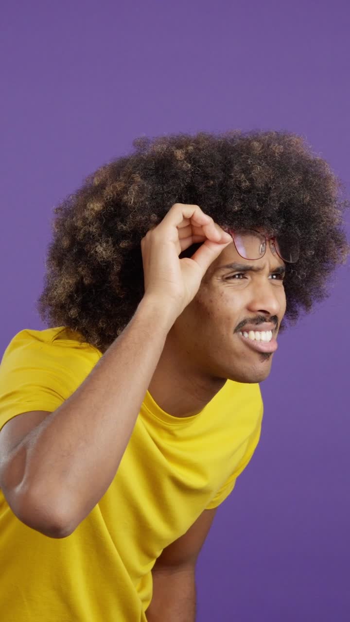 Man with afro and mustache squinting through glasses on purple background