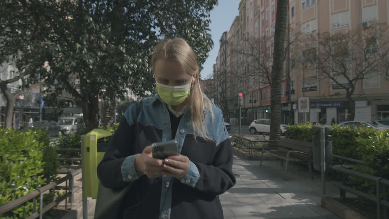 Woman in mask walking in the street being attracted to mobile