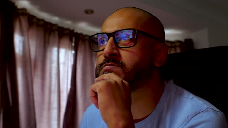 a south asian man working from home, deep in thought with reflections in his glasses