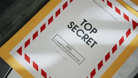 briefcase being opened containing top secret folder with classified documents. retro old looking manila envelope with red label coversheet. government agency suitcase stealing sensitive files and info