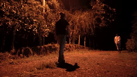 Man-and-woman-take-a-nighttime-walk-through-the-forest-accompanied-by-their-two-dogs