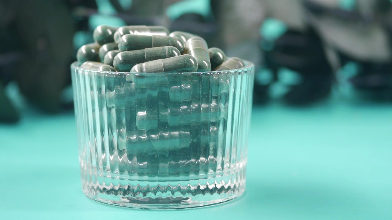 Capsule erboristiche verdi in un bicchiere di vetro su uno sfondo turchese