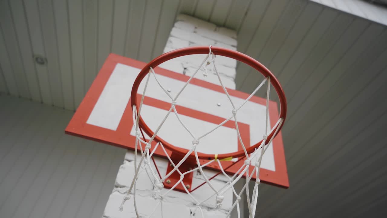 A red basketball net hangs on the white brick wall. The camera shoots in motion.