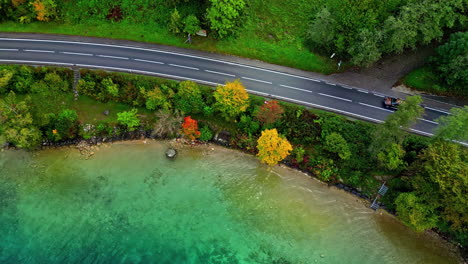 car driving on remote lakeside road, aerial top down view