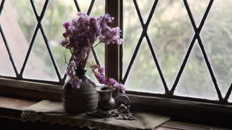 vibrant purple flowers arranged in a rustic vase, placed against an old victorian window