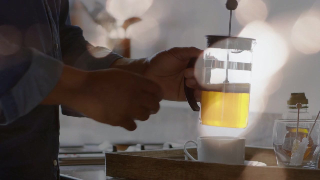 Man entering holding French press, tilting and steadying over cup in kitchen, teaching coffee prep