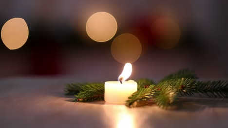 A lit candle with pine branches and blurry lights in the background