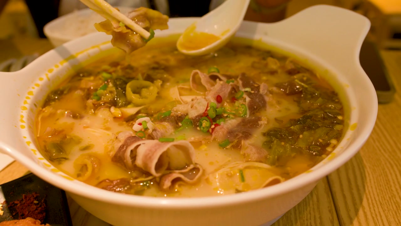 Primo piano di bacchette che prendono carne di manzo da una ciotola fumante di zuppa di noodle asiatica piccante