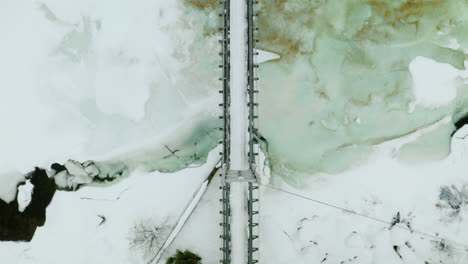 Vista-De-Arriba-Hacia-Abajo-Del-Puente-Colgante-Simple-A-Través-Del-Río-Helado-En-La-Temporada-De-Invierno-En-Haugastol,-Noruega