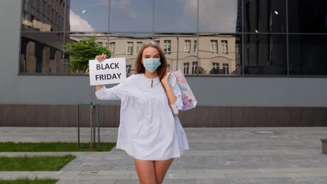 niña con máscara protectora con bolsas de compras que muestran la inscripción de viernes negro durante el coronavirus