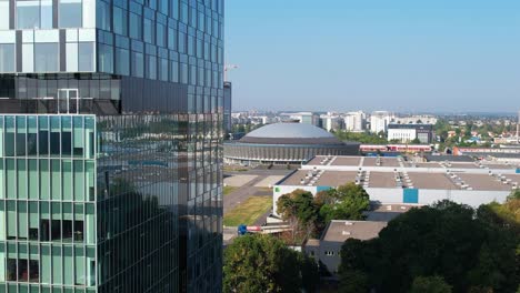 Vista-Aérea-Lateral-De-Un-Edificio-Alto-De-Oficinas-Con-La-Cúpula-De-Romexpo-Al-Fondo,-Bucarest,-Rumania