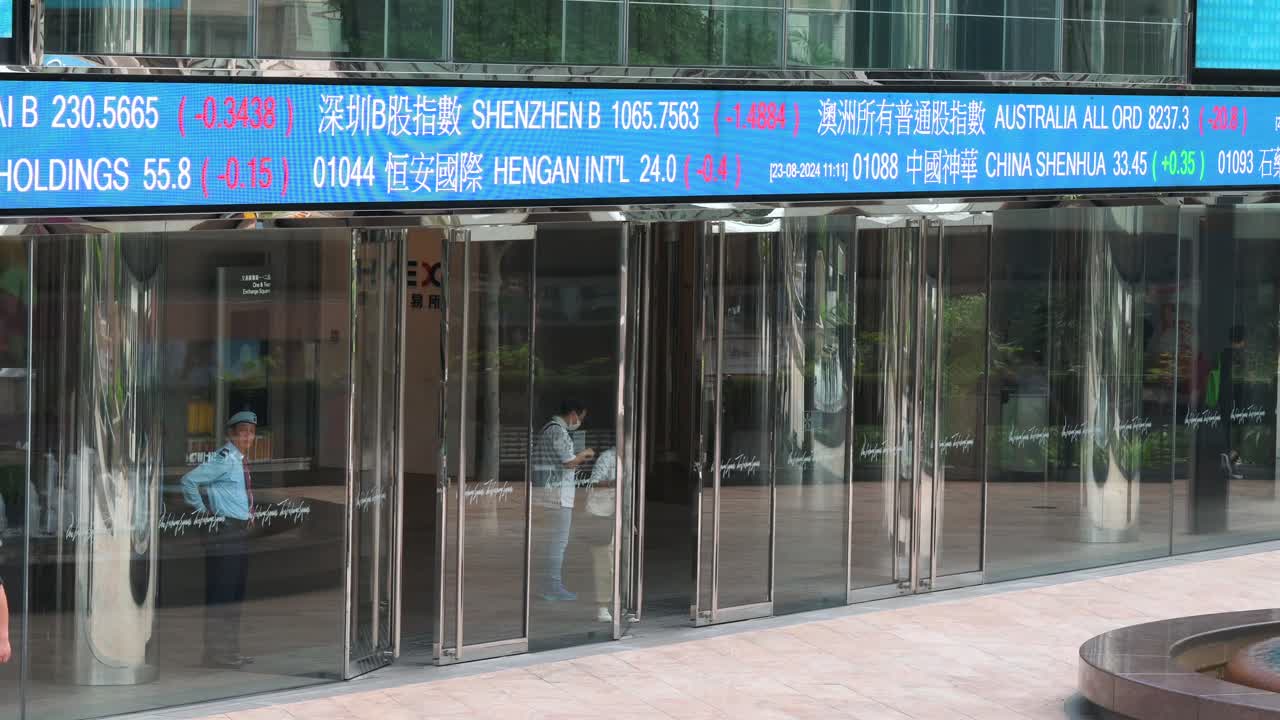 A woman is seen leaving the Exchange Square building, home to the Hong Kong Stock Exchange (HKEX), as a moving screen displays negative stock ticker symbols in Hong Kong’s financial district.