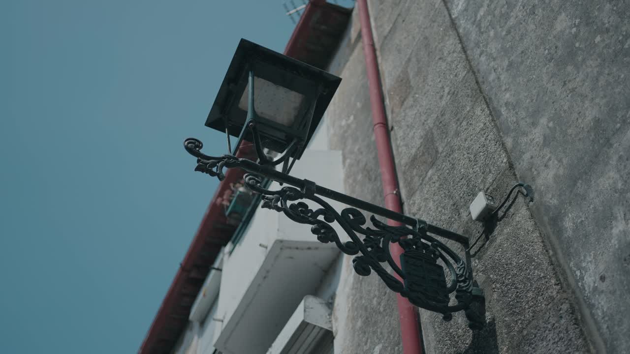 Ornate black iron streetlight mounted on an old stone wall against blue sky