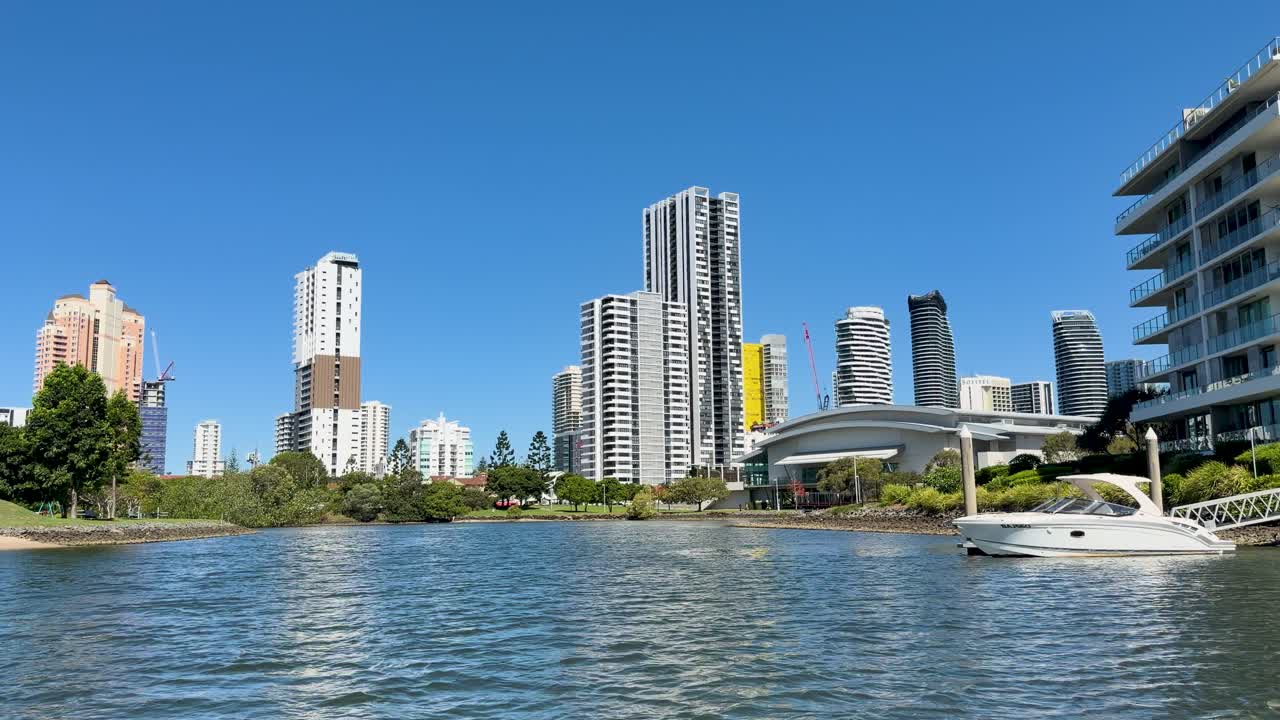 White motorboat glides on river before modern high-rise buildings, sunny day, steady wide shot