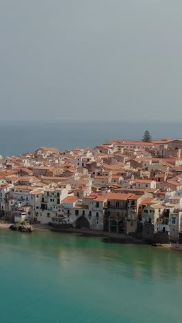 vertical descending aerial drone shot into the bay of cefalu town. sandy beach in a small historic town in sicily.