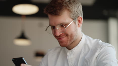 hombre alegre está leyendo un mensaje en el teléfono inteligente o viendo una imagen divertida en las redes sociales durante el día de trabajo en la oficina