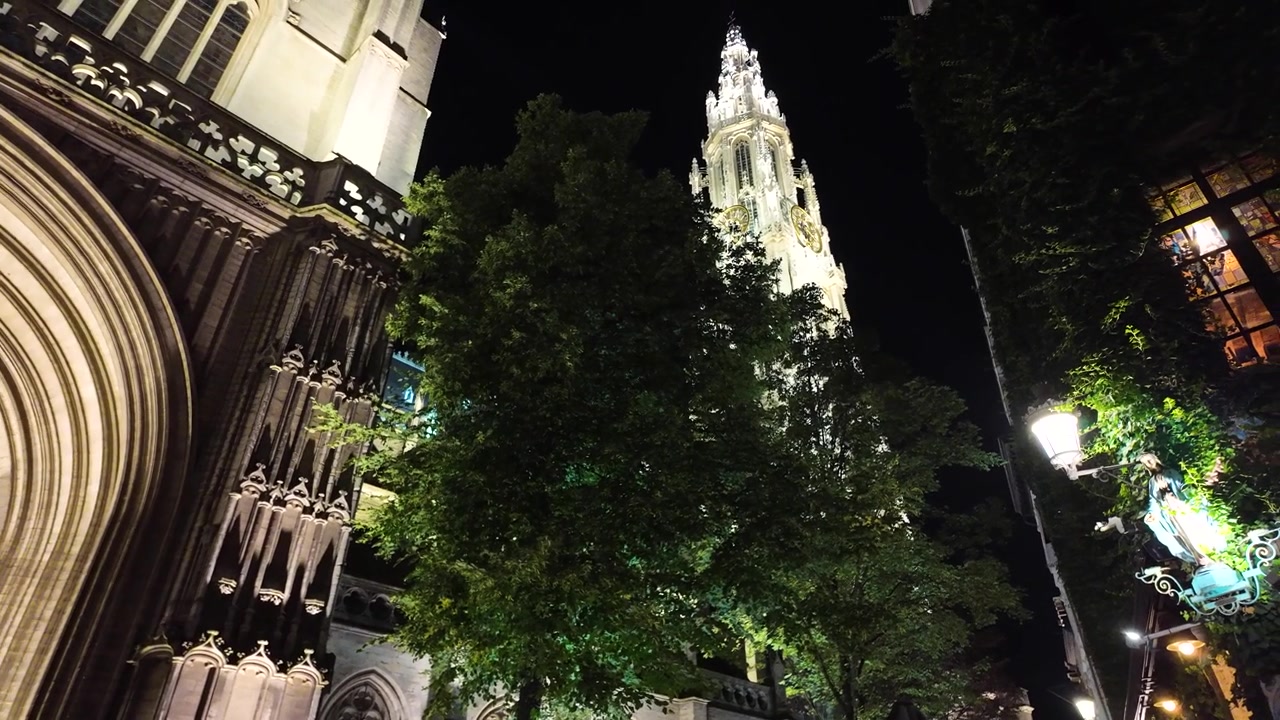 Vista nocturna de la Catedral de Nuestra Señora de Amberes iluminada contra un cielo nocturno dramático.