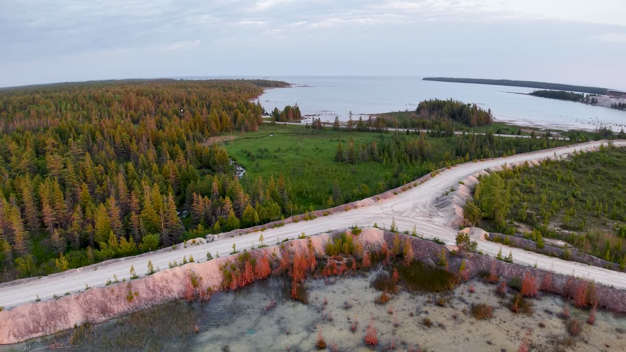 Aerial drone view of a breakwater wall stretching into turquoise coastal waters with a forested shoreline in the distance
