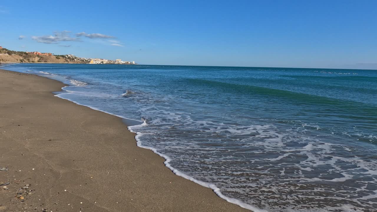Onde che si infrangono dolcemente lasciano una scia bianca sulla spiaggia sabbiosa mentre l'acqua si ritira