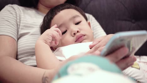 asian baby using smartphones with mom on the bed