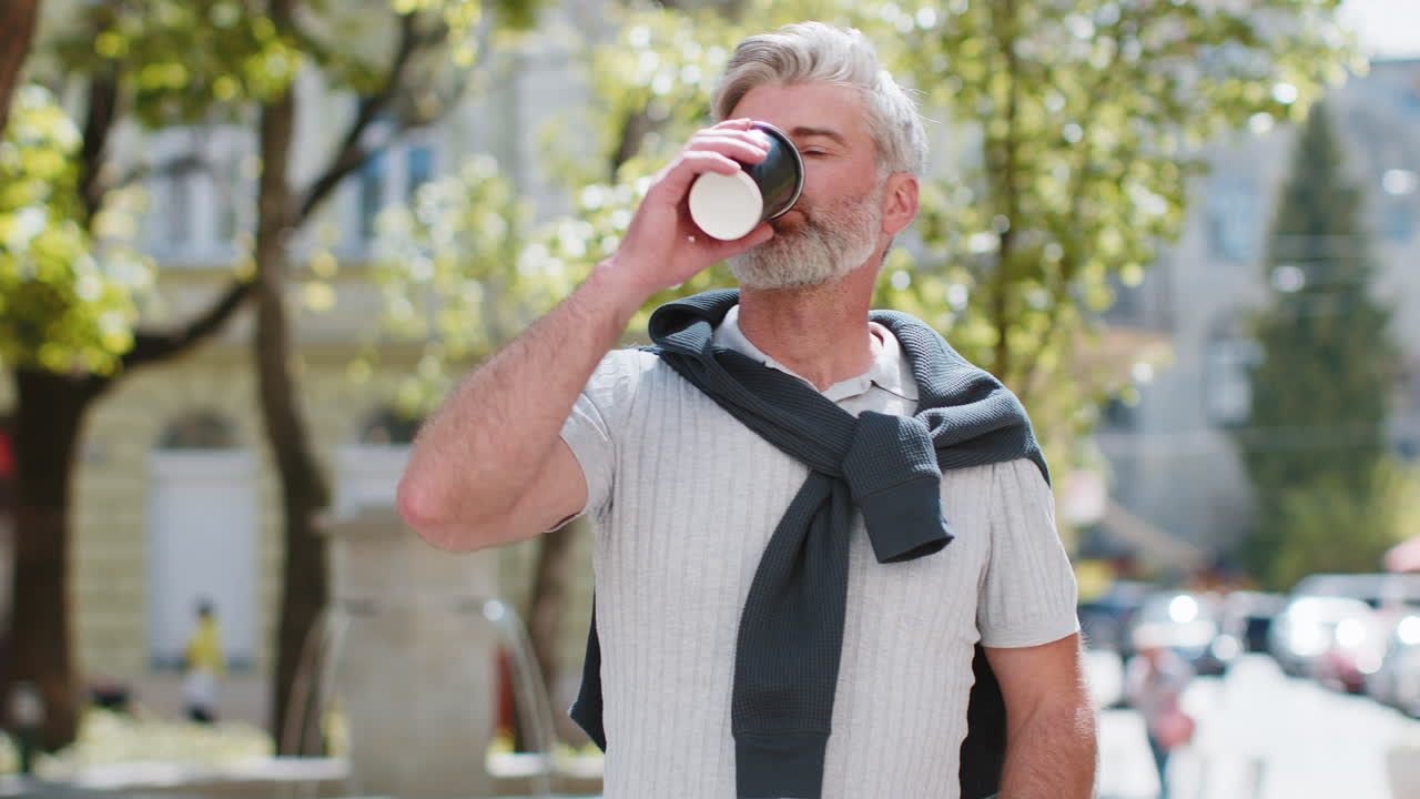 feliz hombre maduro sonriente disfrutando del café de la mañana bebida caliente relajante caminando por la calle de la ciudad urbana