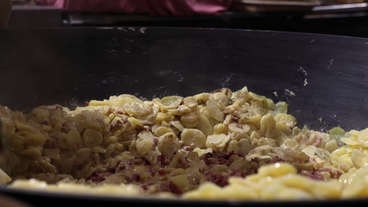 Trabajador de puesto de comida mezclando una gran cazuela de patatas en una sartén