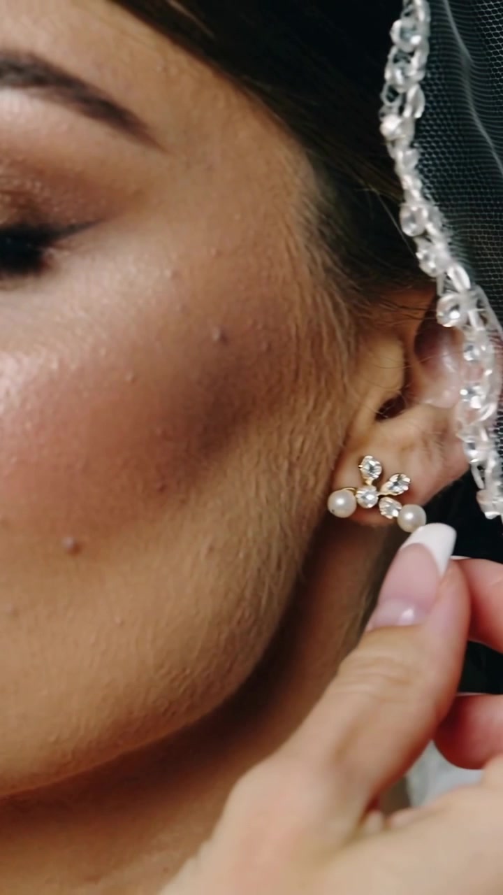 Video verticale: Spostamento della telecamera, profilo della sposa mentre una mano sistema il velo per il matrimonio, orecchino e trucco.