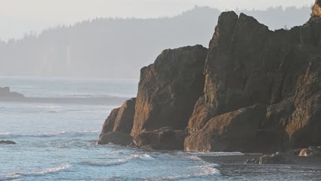 crashing waves against towering sea stacks along a misty forested coastline
