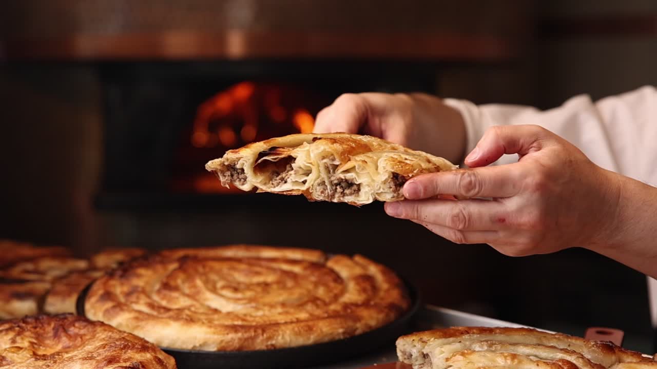 Mani che tengono una fetta di Burek di carne appena sfornato
