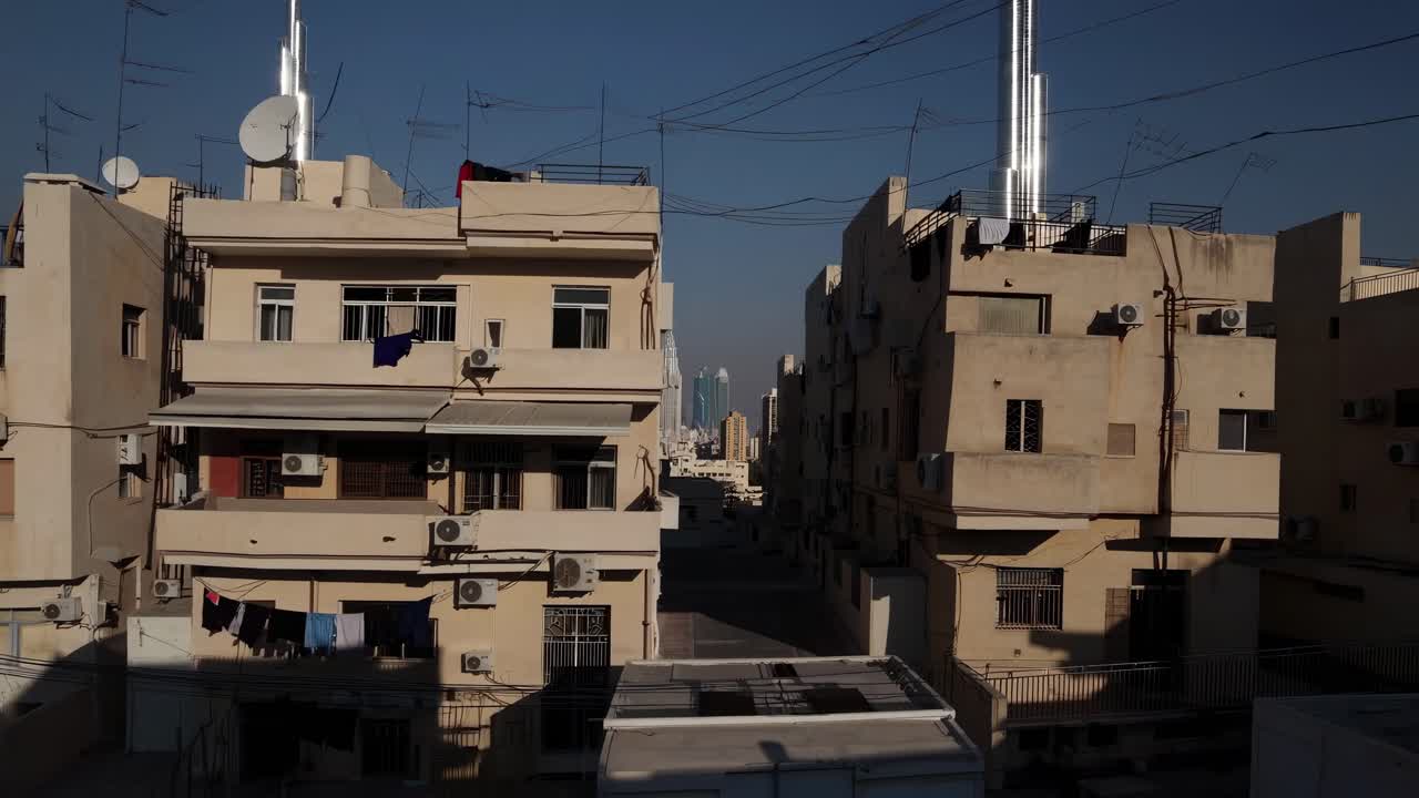 Residential buildings with laundry hanging to dry stand in stark contrast to towering skyscrapers in the background, symbolizing socioeconomic disparities and urban development challenges